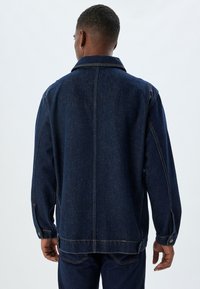 Giacca di jeans blu scuro con colletto, maniche lunghe e polsini con bottoni. Presenta cuciture a vista e un taglio dritto.
