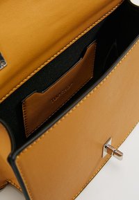 Interno di una borsa in pelle marrone con una foderatura in tessuto nero, dotato di una tasca per carte e dettagli in metallo argentato. Texture liscia, design strutturato.
