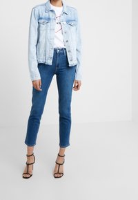 Vaaleansininen farkkutakki, jossa on nappikiinnitys ja hapsureunat, yhdistettynä sinisiin skinny-farkkuihin. Mustat korolliset sandaalit täydentävät asua.