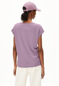 Purple cotton t-shirt with rolled sleeves, featuring a relaxed fit and rounded hem. Paired with a matching cap. Soft texture, minimal design.