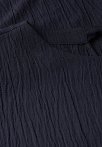 Marinblått texturerat tyg med en rynkad yta, med en konturerad halsringning och en synlig fickdetalj.