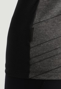 Sportovní tričko s texturovaným šedým základem a černými síťovanými detaily. Na bočním švu jsou vodorovné pruhy, které přidávají na designu.