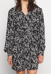Robe portefeuille noire présentant un motif abstrait de vagues blanches, manches longues, taille cintrée et tissu doux et texturé.