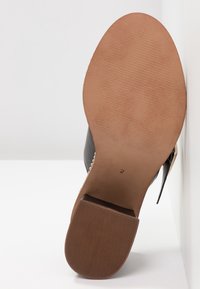 Vue de la semelle d'une chaussure à talon haut noire avec une semelle lisse couleur tan, un bout de talon texturé et un petit numéro de taille imprimé "2" près de la voûte plantaire.