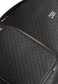 Μαύρο σακίδιο από δερμάτινη υφή με ανάγλυφο σχέδιο, χρυστό φερμουάρ και μικρό χρυσό λογότυπο στην επάνω δεξιά γωνία.