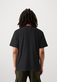 Camiseta de algodón negra con cuello redondo, mangas cortas y un logotipo sutil impreso en la parte superior de la espalda. Textura suave y corte relajado.