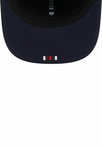 Marineblaue Baseballmütze mit flachem Schirm, die ein kleines rot-weiß-schwarzes Emblem auf der Vorderseite trägt. Glattes Material und strukturierte Form.