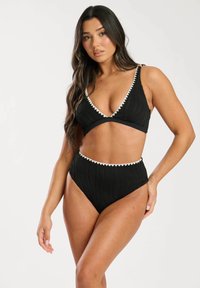 Set bikini nero con un design testurizzato e bordo ondulato bianco a contrasto, composto da un top triangolare e un bottom a vita alta.