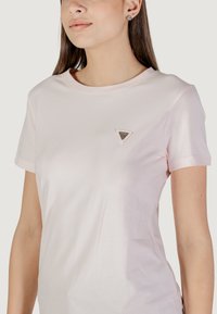 T-shirt a maniche corte rosa chiaro realizzato in tessuto morbido. Presenta un logo a triangolo nell'angolo in alto a sinistra. Girocollo e taglio aderente.