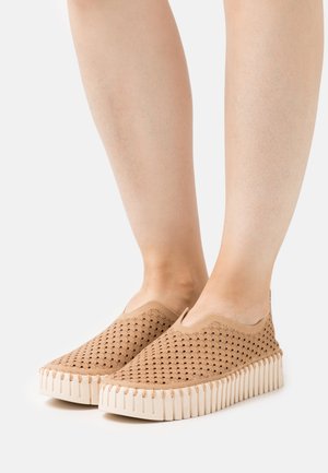 Scarpe slip-on beige con tomaia in tessuto perforato e suola in gomma testurizzata, caratterizzate da bordi ondulati e un design a profilo basso.