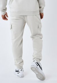 Pantalones cargo de sudadera gris claro hechos de una tela suave, con bolsillos laterales y puños elásticos, combinados con zapatillas blancas con un logotipo negro.