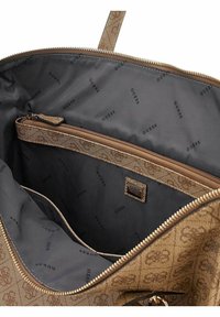 Intérieur d'un sac à main à motif marron avec une doublure noire lisse, une poche zippée avec une fermeture éclair métallique et des embellissements de logo.