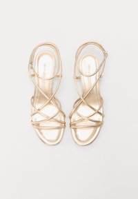 Sandales dorées à lanières avec un design plat, une finition métallique et une semelle intérieure rembourrée, dotées de lanières croisées et d'une boucle à la cheville.