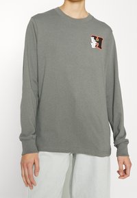 Langärmliges graues T-Shirt aus weicher Baumwolle; mit einem gestickten Charakter- und Buchstabendesign auf der linken Brust; runder Halsausschnitt und lockere Passform.