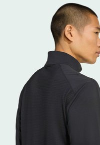 Black athletic jacket with a high collar, textured pattern, and a fitted design. Features smooth fabric and a clean, streamlined silhouette.