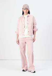 Chaqueta de denim rosa con dos bolsillos frontales y jeans de pierna ancha rosa a juego. Usada con un suéter blanco y una gorra beige. Tejido texturizado.
