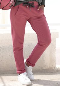Rosa Sweatpants mit Kordelzugbund, seitlichen Taschen und umgeschlagenen Säumen, kombiniert mit weißen Sneakers auf einer strukturierten Betonoberfläche.
