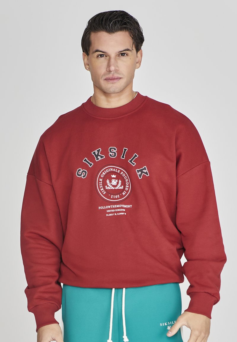 Felpa rossa con collo a girocollo a costine, con stampa di testo e logo bianchi sul fronte. Include maniche ampie e uno stile casual.