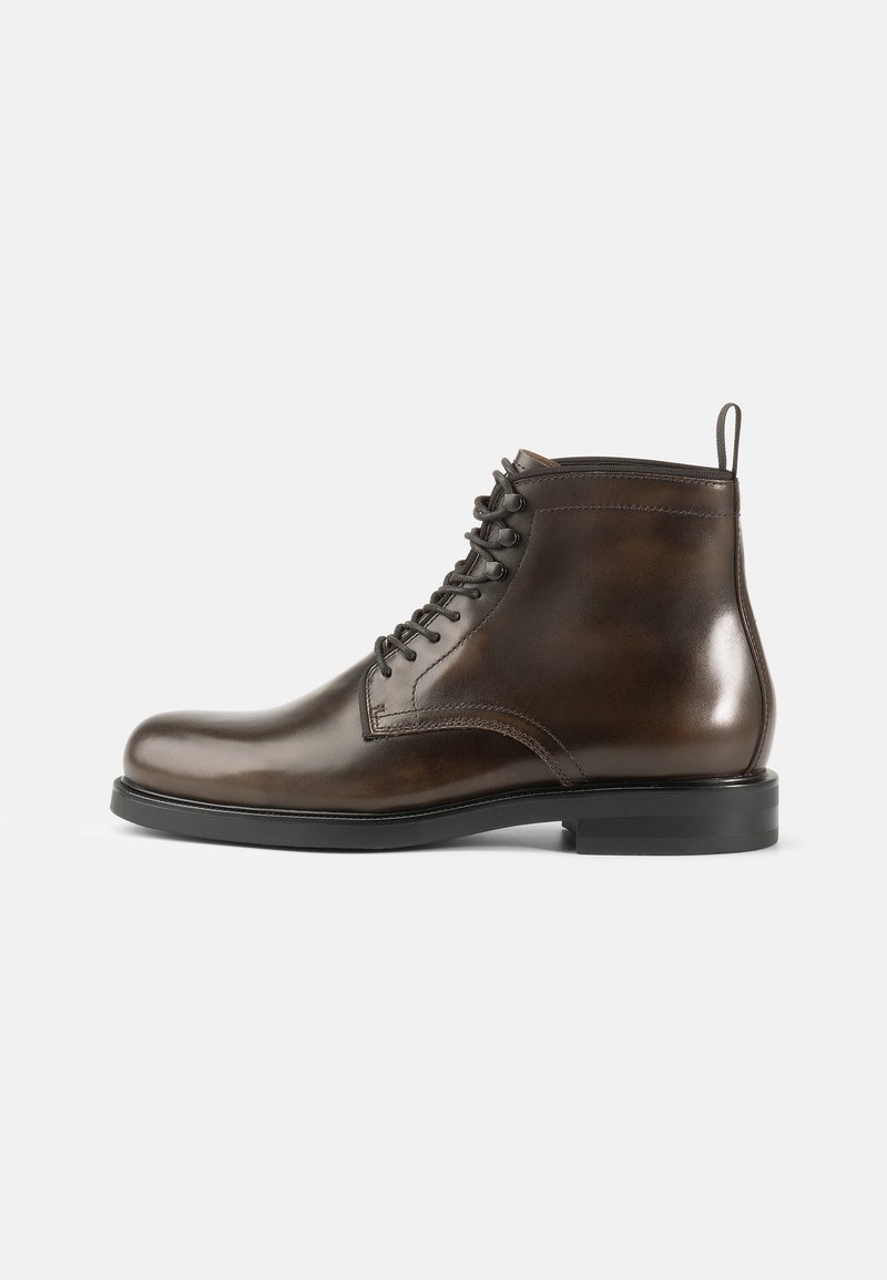 Stivali alla caviglia in pelle marrone con finitura liscia, punta rotonda, design con lacci e suola in gomma nera. Presentano una maniglia sul retro.