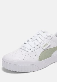 Bílé tenisky s perforovaným svrškem, zelenými akcenty, plochými šňůrkami a silnou gumovou podrážkou. Logo Puma na boku, materiál z texturované kůže.