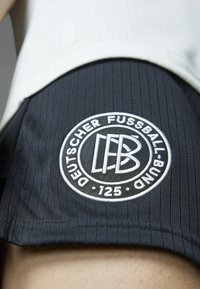 Black sports shorts feature a ribbed texture and a circular white embroidered logo with "Deutscher Fussball-Bund" and "125."