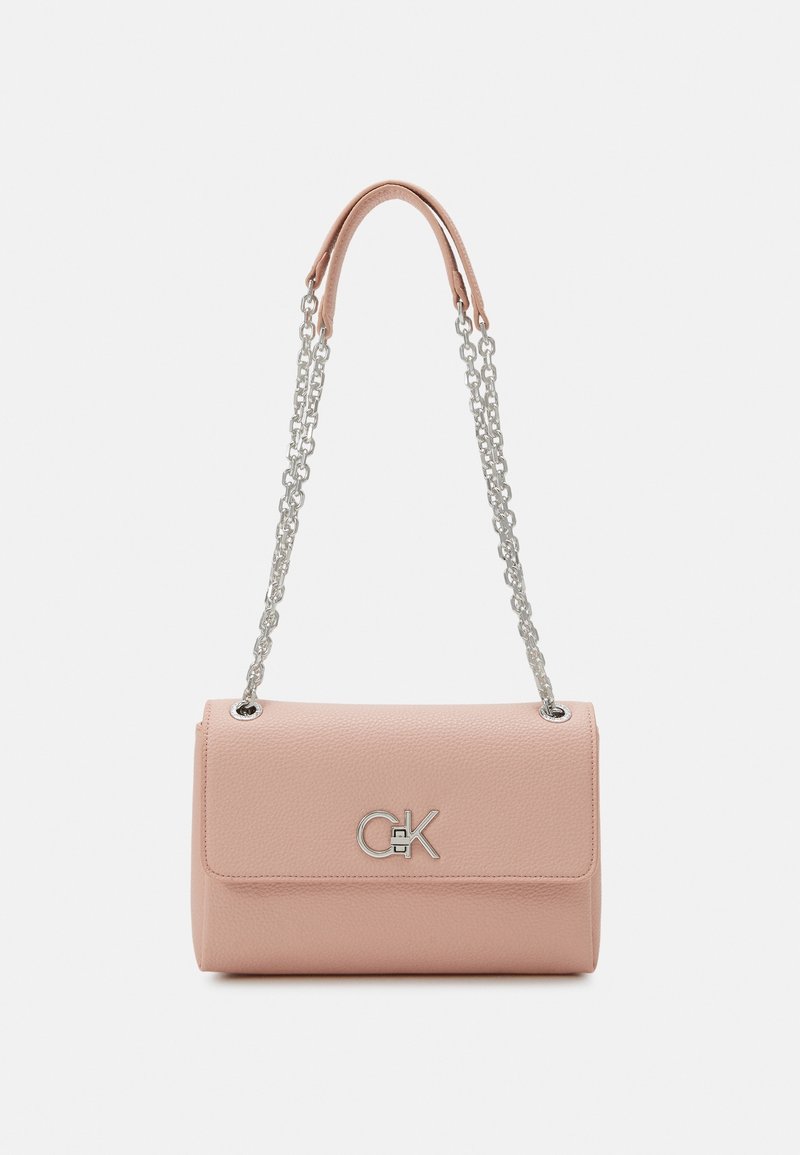 Sac à main en cuir rose blush avec bandoulière chaîne argentée et logo "CK" argenté sur le rabat avant, sur fond blanc uni.