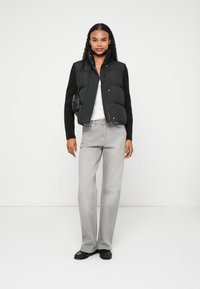 Črn puhasti brezrokavnik preko bele majice, v kombinaciji s svetlo sivo širokimi kavbojkami in črnimi čevlji. Zanj je značilna majhna torbica in strukturirani rokavi.