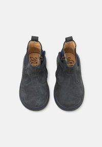 Botines de ante azul oscuro con una textura suave, cremalleras laterales y acentos en azul oscuro en contraste. Punta redondeada y detalles de costura.