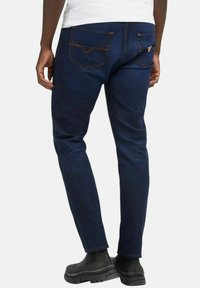 Jeans in denim blu scuro con vestibilità affusolata, dotati di due tasche posteriori, cuciture visibili e un branding sottile sulla tasca destra.