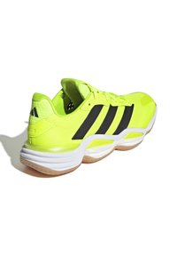 Zapatilla deportiva de color amarillo neón con parte superior de malla, rayas negras, suela blanca acolchada y suela de goma, con un diseño de cordones y cuello acolchado.