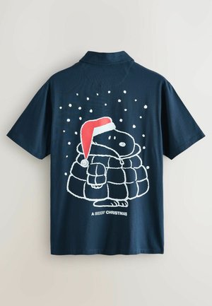 Marineblaues Kurzarmhemd mit einem Grafikdesign eines Cartoon-Hundes, der einen roten Hut und einen Daunenmantel trägt, umgeben von Schneeflocken und dem Text "Ein Snoopy-Weihnachten" darunter.