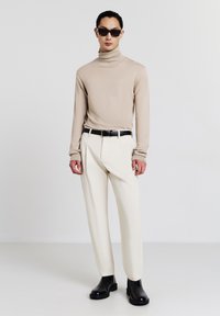 Beige turtleneck top, cream tailored pants, black belt, and black ankle boots. Model wearing dark square sunglasses, minimalistic style.