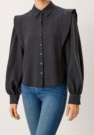 Sort langærmet skjorte med knapper, store skulderpuder og puffede ærmer, båret med blå denimjeans.