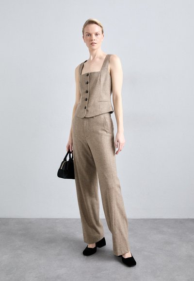 Beige linen blend suit with a sleeveless, square-neck vest featuring black buttons and wide-leg trousers; paired with a small black handbag.