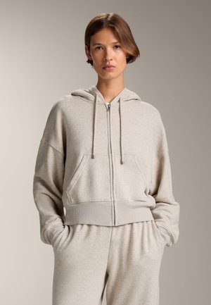 Lichtgrijze zip-up hoodie met een kangoeroezak, een trekkoord voor de capuchon en een ribgebreide zoom. Zachte stof met een ontspannen pasvorm en een ontwerp met verlaagde schouders.