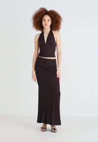 Brūns halter top un pieguļošs maxi svārki, kas izgatavoti no mīksta, elastīga auduma. Iezīmēts ar dziļu dekoltē un šauru siluetu ar ručinga detaļām.