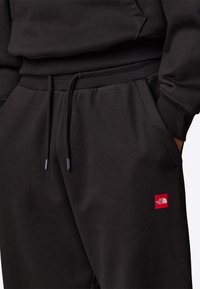 Czarne dresy z elastycznym pasem, sznurkiem, bocznymi kieszeniami i małą czerwoną łatką z logiem The North Face z przodu.