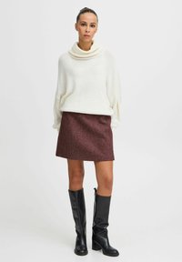 Krém színű, oversized kötött pulóver, cowl nyakkal, egy bordó, texturált mini szoknyával párosítva. Fekete térd fölé érő bőr csizmák egészítik ki a szettet.