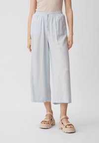 Pantaloni larghi di colore azzurro chiaro realizzati in tessuto morbido e fluido. Presentano un elastico in vita con cordoncino. Texture liscia e taglio alla caviglia.