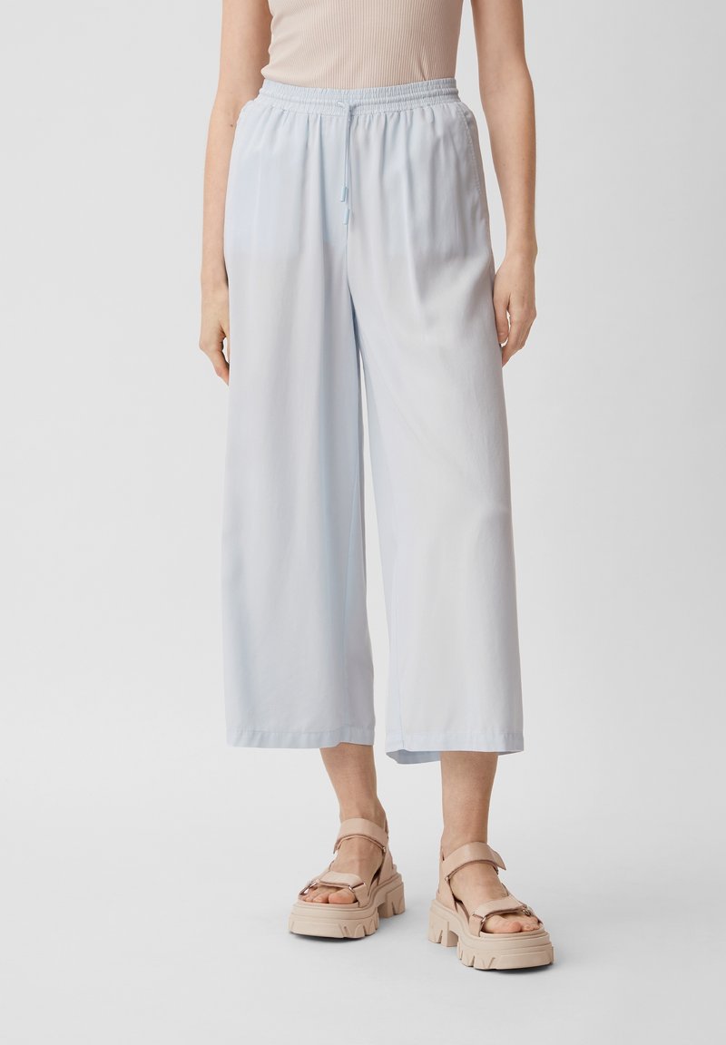 Pantaloni larghi di colore azzurro chiaro realizzati in tessuto morbido e fluido. Presentano un elastico in vita con cordoncino. Texture liscia e taglio alla caviglia.