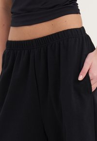 Shorts noirs à taille élastique fabriqués en tissu doux, dotés de poches latérales et d'une coupe décontractée. La texture paraît lisse avec un drapé léger.