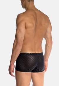 Czarne spodenki kąpielowe z geometrycznym wzorem, wykonane z gładkiego, półprzezroczystego materiału, prezentujące dopasowany krój i elastyczną talię.