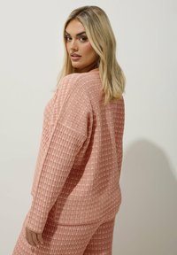 En strukturerad rosa långärmad topp med en fyrkantig form och lös passform, med ribbade detaljer och ett subtilt rutmönster.