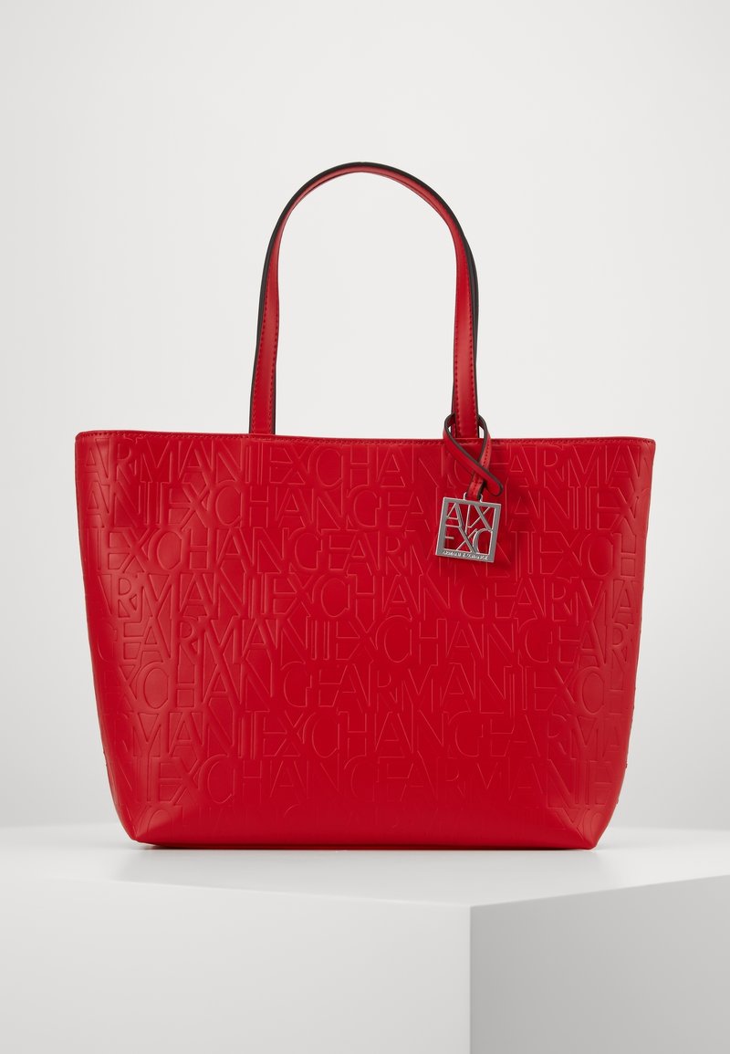 Sac cabas rouge avec texte embossé « Armani Exchange » partout et un charm argenté de marque suspendu à une poignée.
