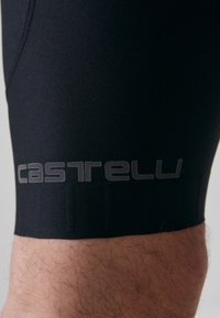 Shorts de cyclisme noirs en tissu extensible, avec une texture douce et un logo "castelli" gris bien visible près de l'ourlet.