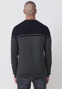 Suéter de punto con un cuerpo texturizado en gris oscuro y una parte superior lisa en azul marino, adornado con una delgada franja gris a través de los hombros.