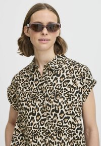 Camicia con stampa leopardata, colletto a punta, maniche corte e chiusura a bottoni. Modello con occhiali da sole color viola.