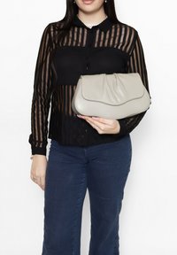 Clutch in pelle grigia con una chiusura a pattina arricciata, tenuta in mano. La borsa presenta una texture liscia e una forma arrotondata, offrendo un'eleganza sobria.