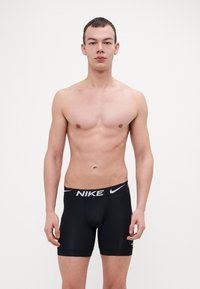 Fekete Nike boxer alsónadrág, szoros szabással, széles derékkal, amelyet a Nike logó díszít, és puha, sima anyagtextúrával rendelkezik.