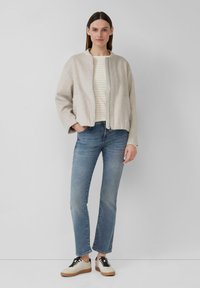 Light beige zip-up jacket, striped cream and beige top, blue straight-leg jeans, and beige sneakers with black laces. Smooth texture overall.